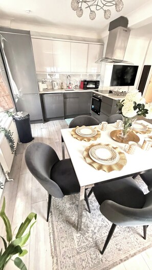 A modern kitchen with a dining area, including a table set with plates and a vase of flowers. - Apartment Sleeps 11 With Air Conditioning (London)