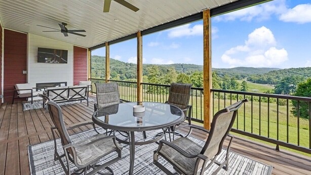 A covered outdoor area with a table and chairs, a ceiling fan, and a view of a green landscape.