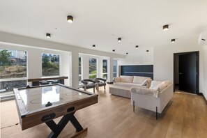 A modern living space with a pool table, seating area, and large windows. - Bear Mountain Retreat | AC | 400 Sq Ft Patio | Golf & Resort-Style Amenities (Victoria)