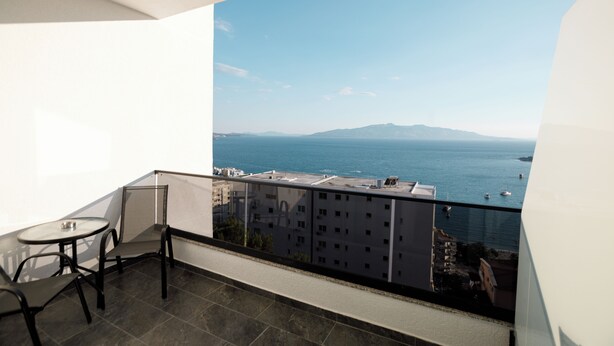 A balcony with a table and chairs, overlooking a body of water and distant mountains.