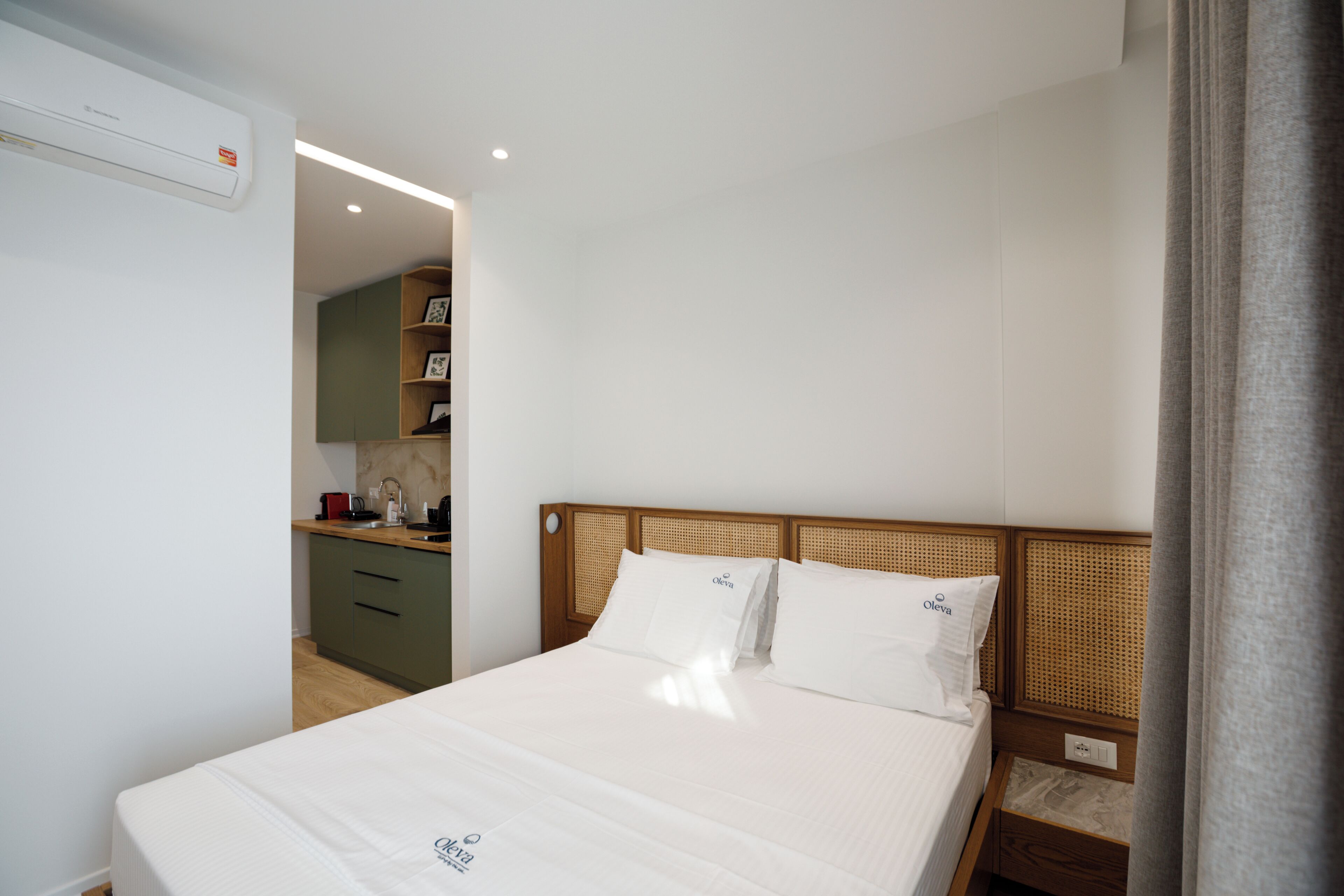 Habitación de hotel con cama, mesita de noche, cabecera de madera, una pequeña mesa, kitchenette y baño.