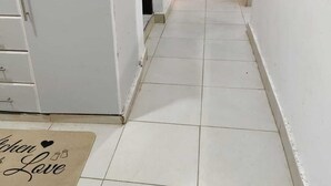 A narrow kitchen corridor with white cabinets, a microwave, and a wooden door at the end. - J & M Homes 2 bedroom unit (Naivegas apartment) (Naivasha)