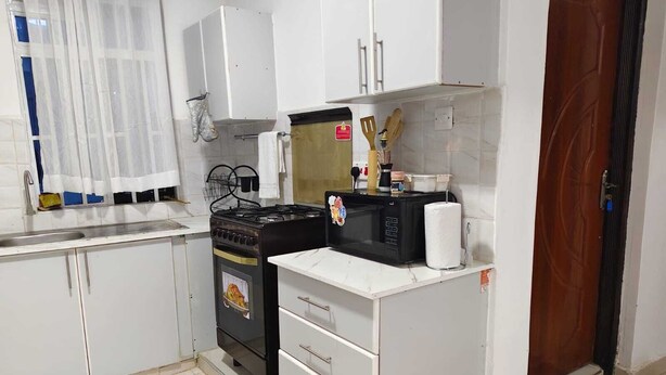 A kitchen with white cabinets, a stove, a microwave, and a wooden door. - J & M Homes 2 bedroom unit (Naivegas apartment) (Naivasha)