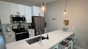 Una cocina moderna con armarios blancos, electrodomésticos de acero inoxidable, una isla central con taburetes altos e iluminación colgante.