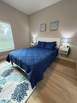 A bedroom with a bed, two bedside tables, a window with blinds, and a wall with two framed pictures. - Gorgeous Coastal Townhome - 8 min from Boca Grande, Close to Beaches & Shops (Port Charlotte)