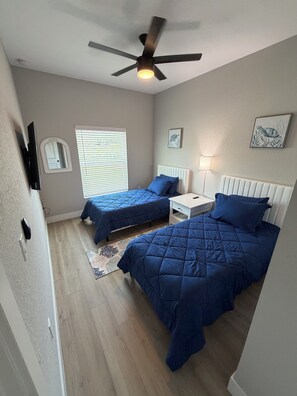 A bedroom with two beds, a ceiling fan, a window with blinds, and a bedside table with a lamp. - Gorgeous Coastal Townhome - 8 min from Boca Grande, Close to Beaches & Shops (Port Charlotte)