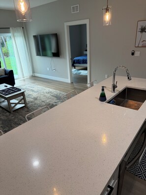 A modern kitchen with a large island, a built-in sink, and a flat-screen TV mounted on the wall. - Gorgeous Coastal Townhome - 8 min from Boca Grande, Close to Beaches & Shops (Port Charlotte)