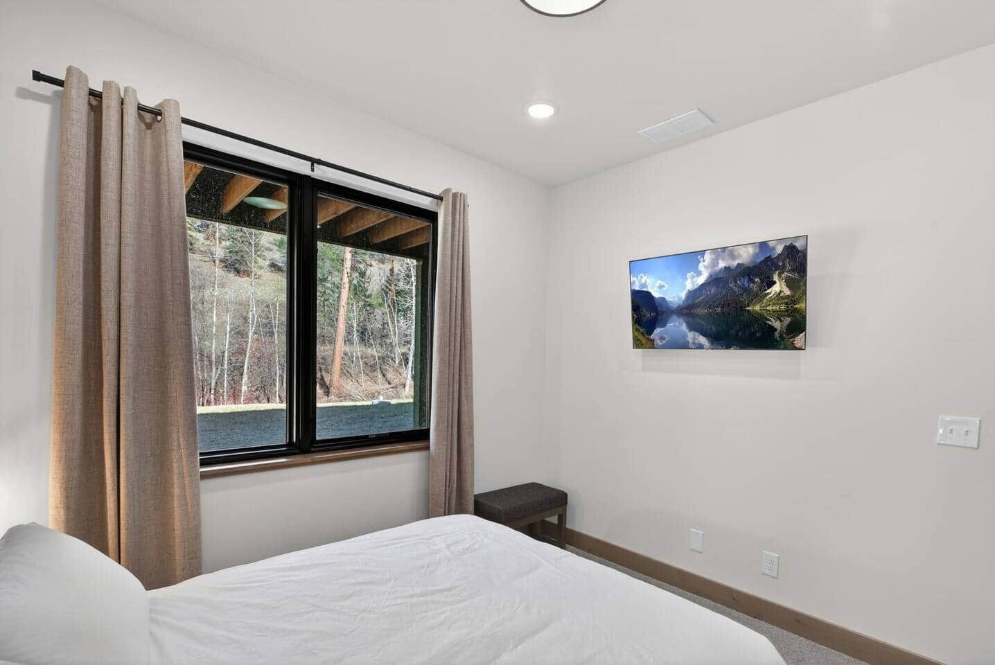 Een slaapkamer met een bed, een raam met gordijnen, een klein nachtkastje en een aan de muur hangend schilderij.