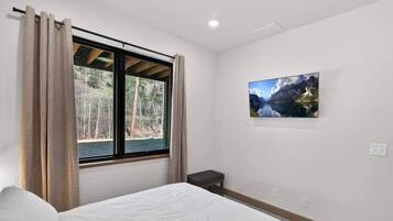 Een slaapkamer met een bed, een raam met gordijnen, een klein nachtkastje en een aan de muur hangend schilderij.