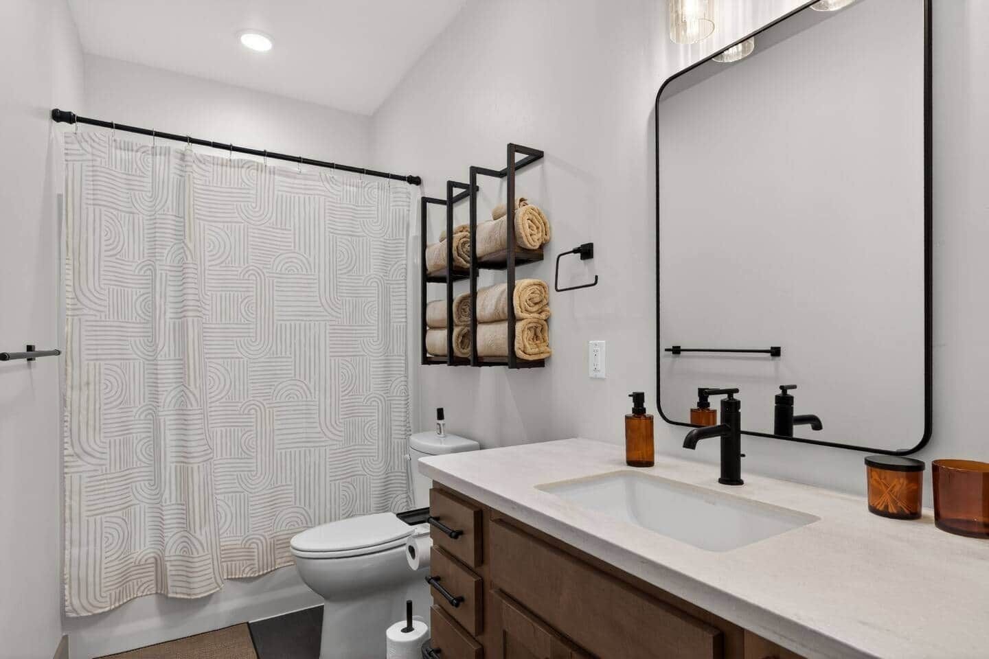 Un baño moderno con cortina de ducha, inodoro, tocador con espejo y barra para toallas.