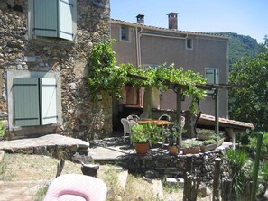 A stone building with a garden area featuring potted plants and a pergola with vines. - Country House, Cévennes 30 (Gard) (Saint-Laurent-le -Minier)