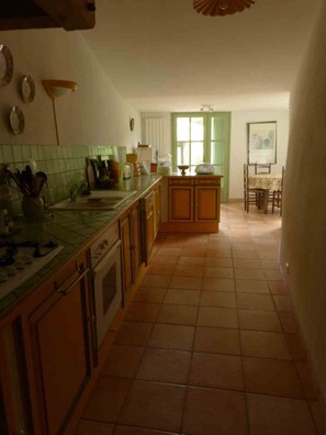 A kitchen with a tiled floor, wooden cabinets, a countertop, and a dining area with a table and chairs. - Country House, Cévennes 30 (Gard) (Saint-Laurent-le -Minier)