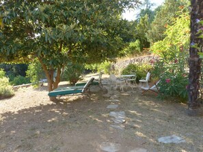 An outdoor seating area with a stone wall, a tree providing shade, and a view of a garden. - Country House, Cévennes 30 (Gard) (Saint-Laurent-le -Minier)