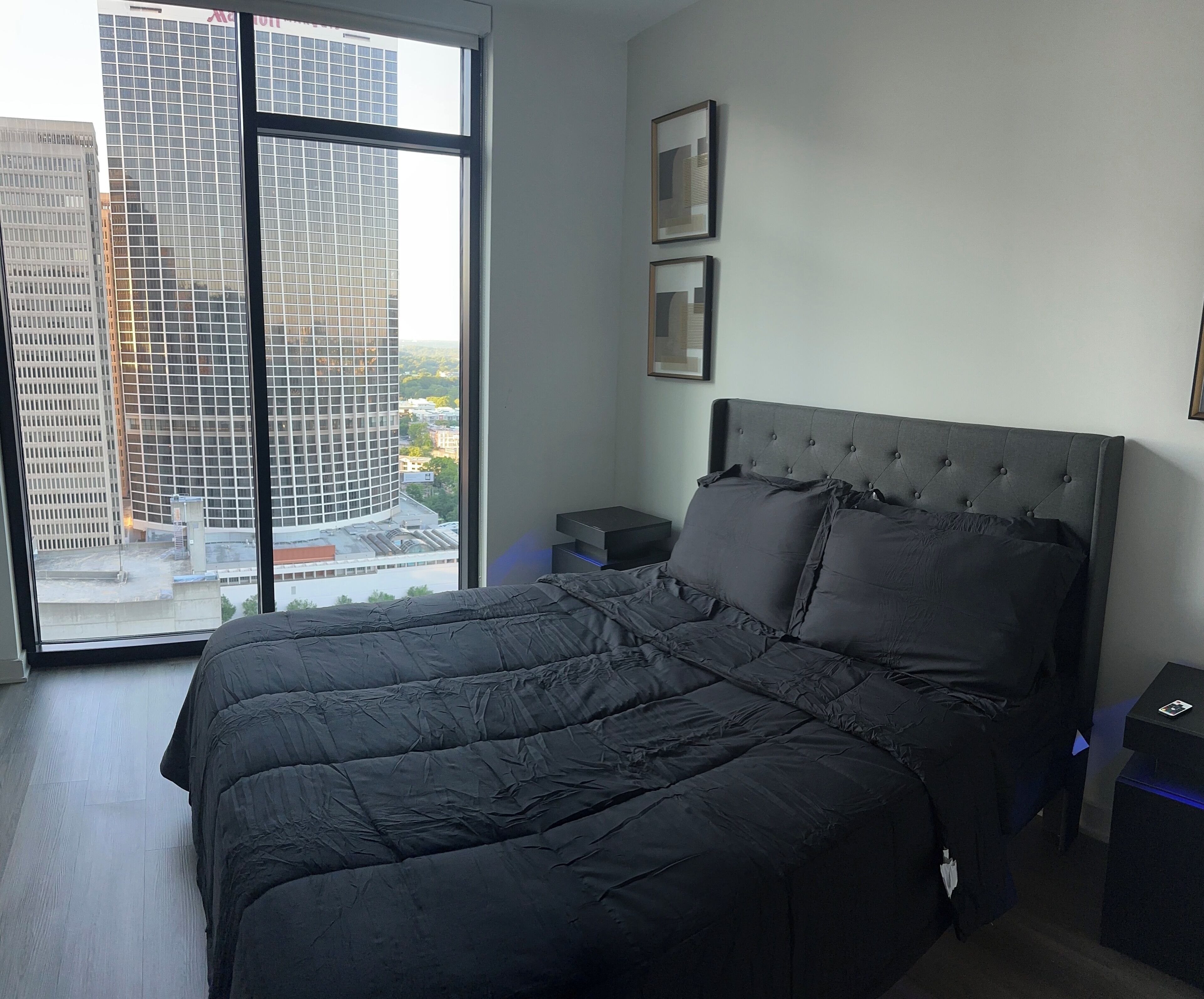 Ein Schlafzimmer mit einem großen Bett, einem Nachttisch, einer Kommode und einem Fenster mit Blick auf die Stadt.