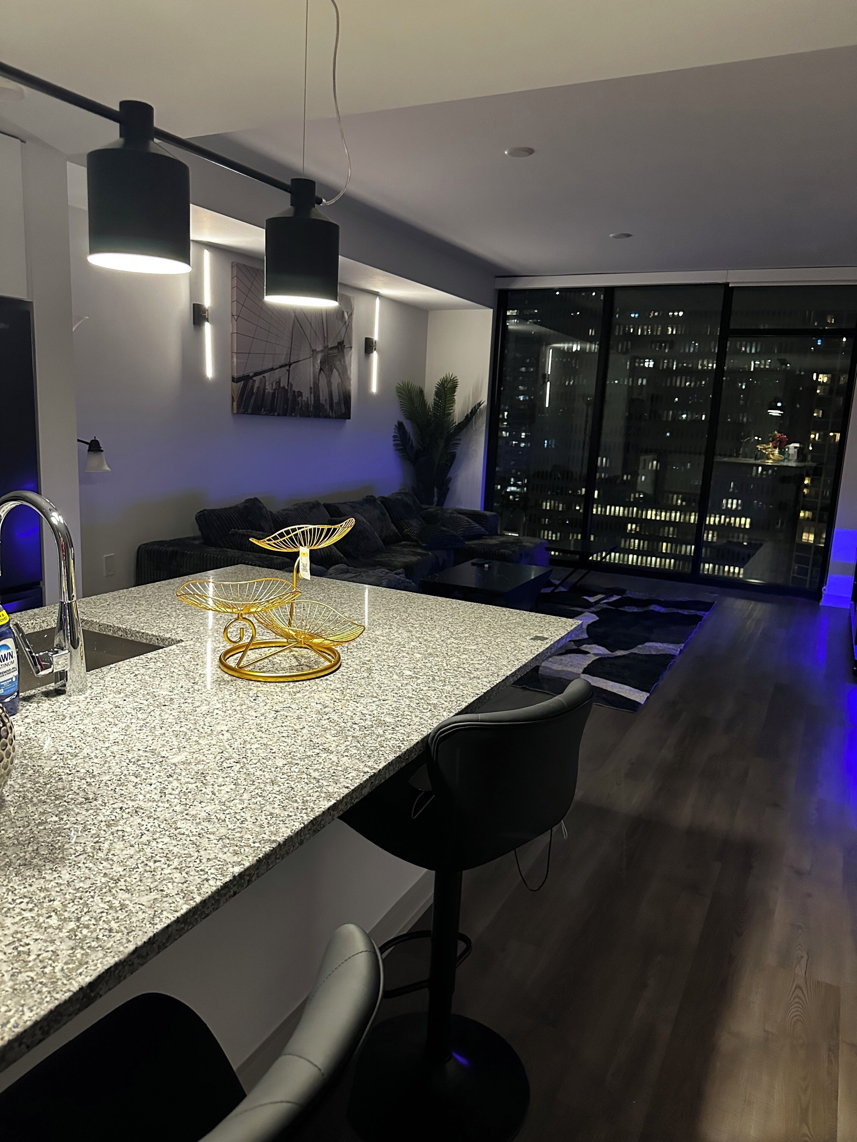 A modern kitchen with a granite countertop, black bar stools, and pendant lighting.