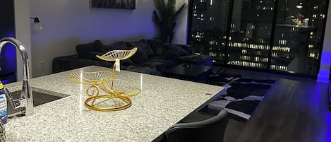 A modern kitchen with a granite countertop, black bar stools, and pendant lighting.