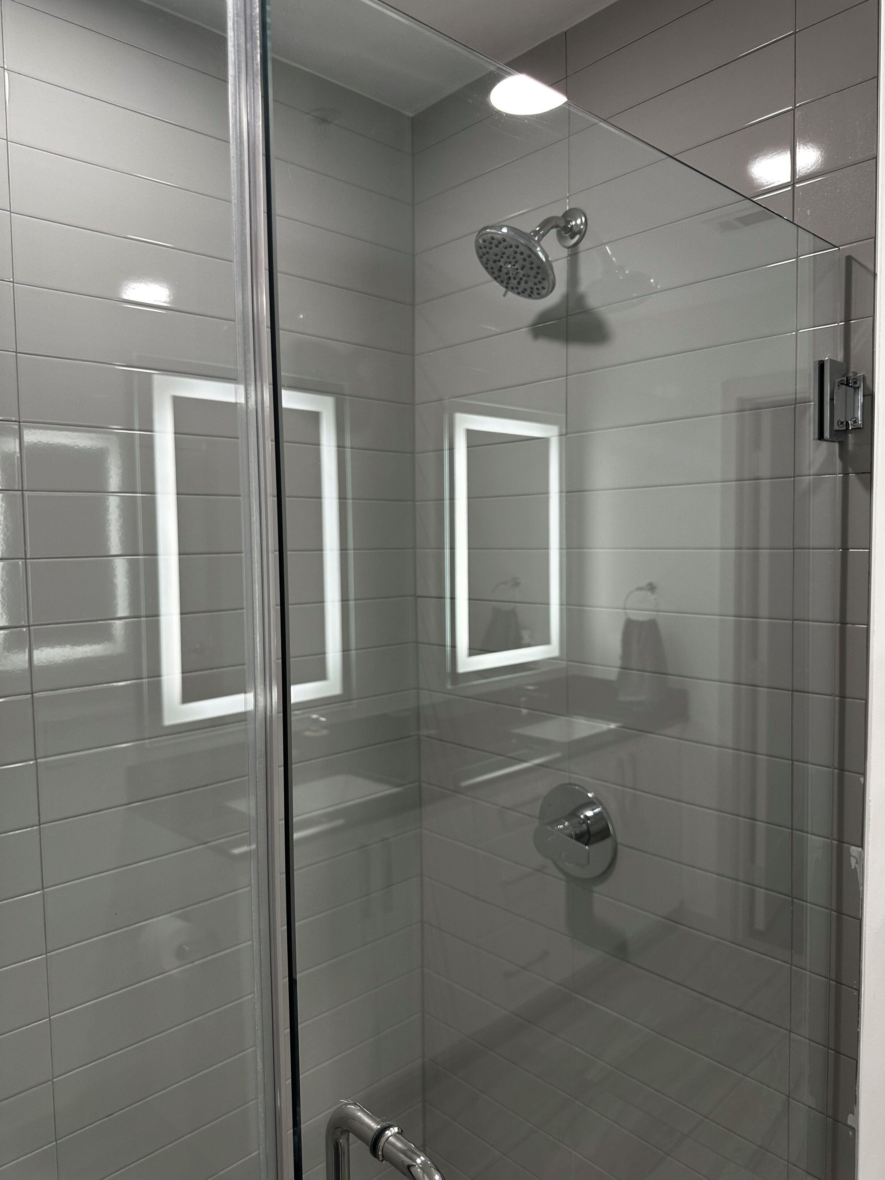 Une salle de bain moderne avec une douche à parois de verre, des toilettes apparentes et un miroir.