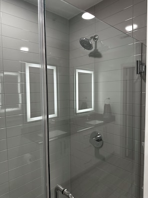 A modern bathroom with a glass shower enclosure, a visible toilet, and a mirror. - Downtown Beauty (Atlanta)