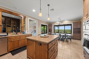 Una cocina amplia con encimeras de granito, gabinetes de madera y una isla grande. Hay un comedor con vistas al exterior.
