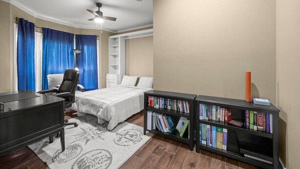 Ein Schlafzimmer mit Bett, Schreibtisch, Stuhl, Bücherregal und Deckenventilator.