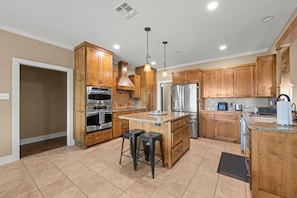 A modern kitchen with wooden cabinets, stainless steel appliances, and a central island with stools. - Wanderers Haven - pool + media room, gatherings (Belton)