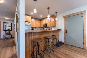 A kitchen with wooden cabinets, a stainless steel refrigerator, a microwave, and three bar stools. - Evergreen Paradise - Hot Tub, Fireplace, Walk to (Crested Butte)