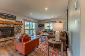 A living room with a stone fireplace, leather sofas, a coffee table, and a large window. - Evergreen Paradise - Hot Tub, Fireplace, Walk to (Crested Butte)