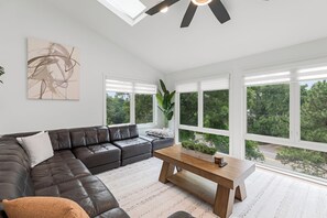 A modern living room with a leather sofa, a wooden coffee table, and large windows with a view of greenery.