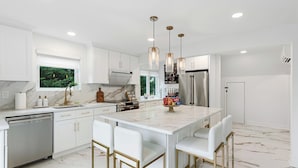 Una cocina moderna con armarios blancos, encimera de mármol y una isla central con taburetes de bar.
