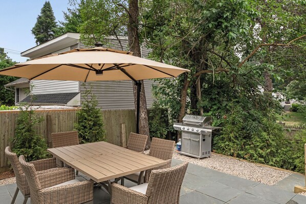 An outdoor patio with a table and chairs, a barbecue grill, and a large umbrella.