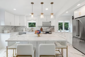 A modern kitchen with white cabinetry, a marble island, and stainless steel appliances.