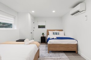 A modern bedroom with two beds, a small bedside table, a potted plant, and an air conditioning unit.