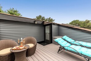 A deck with wicker furniture and a table set with food and drinks.