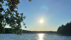 A beach with a wooden bench and a calm lake reflecting the sun. - Lakeside cottage with private beach in Sörmland (Stavsjö)