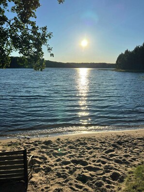 Uma praia com um banco de madeira e um lago calmo refletindo o sol.