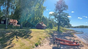 A lakeside property with a wooden dock, a small boat, and a red canoe. - Lakeside cottage with private beach in Sörmland (Stavsjö)