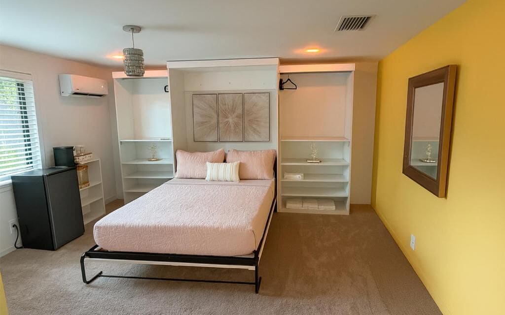 Une chambre à coucher comprenant un lit, des étagères intégrées, un miroir et un petit bureau.