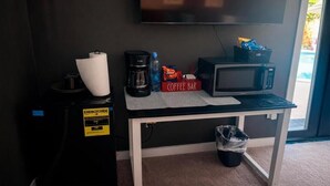 Una pequeña cocina americana equipada con cafetera, microondas y una barra para café sobre la mesa.