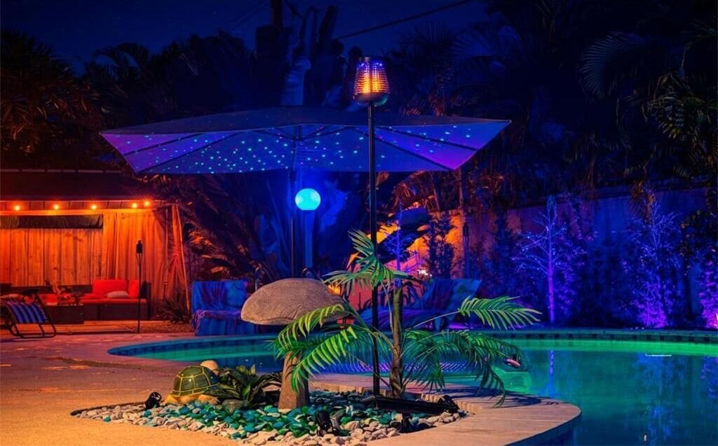 Un área de piscina con sombrilla tiki, palmeras y una lámpara tiki.