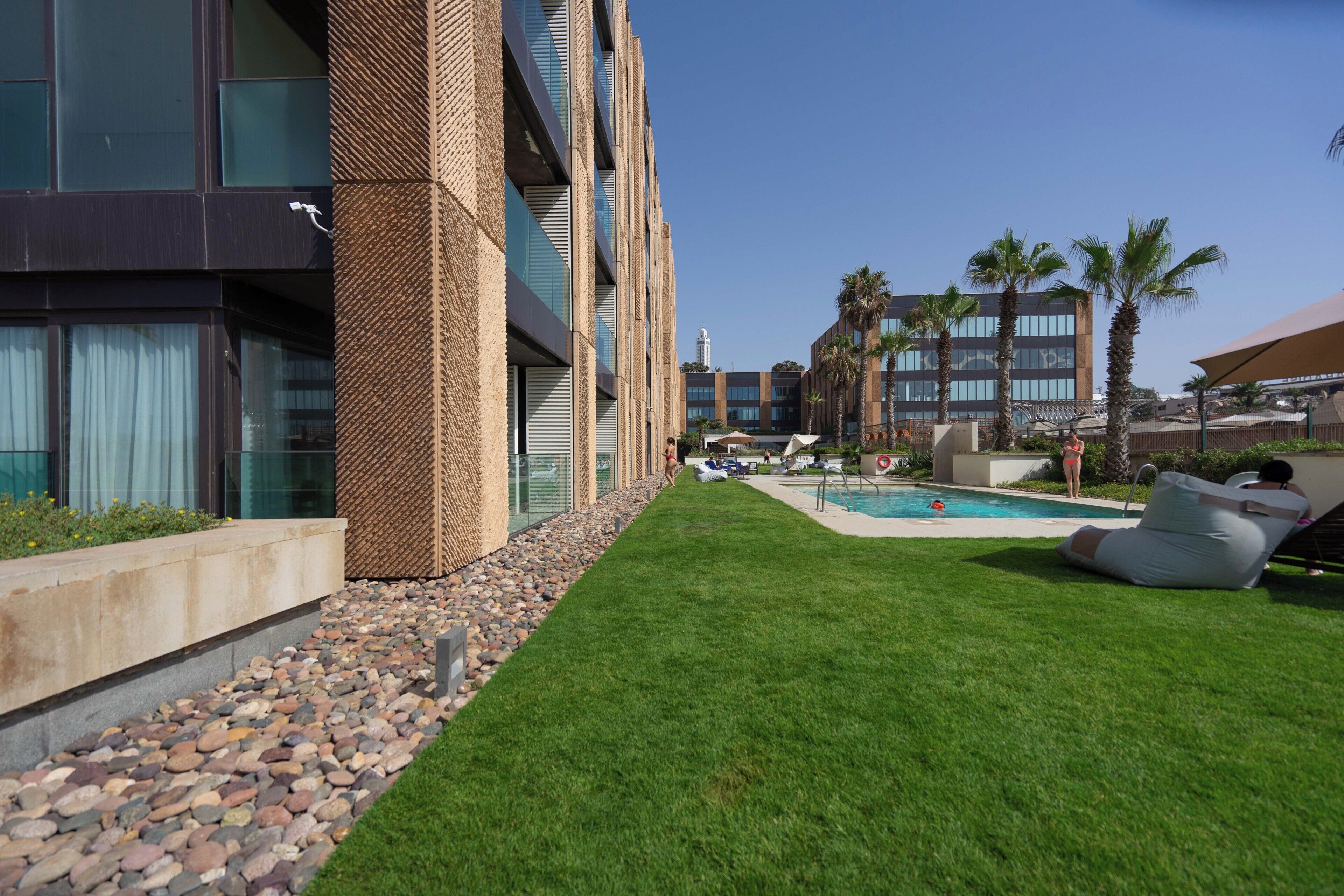 A hotel with a swimming pool, lounge chairs, and a well-maintained lawn.