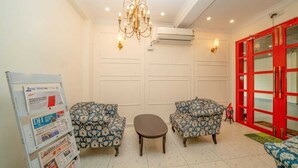 A room with two patterned armchairs, a small table, a chandelier, an air conditioning unit, and a red door. - The Clock Tower Inn (Bengaluru)
