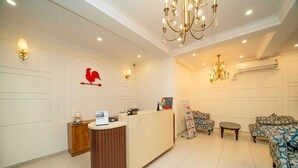 A reception area with a reception desk, two chandeliers, a patterned sofa, and a wall-mounted rooster decoration. - The Clock Tower Inn (Bengaluru)