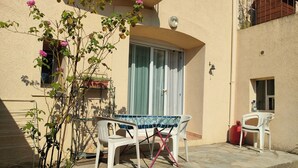 Pieni patio, jossa on pöytä ja tuoleja, ruukussa oleva kasvi ja pieni ikkuna.