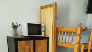 A room with a wooden bunk bed, a small cabinet with a microwave, and a trash bin.