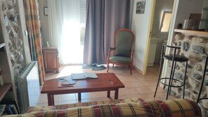 A living room with a sofa, a wooden table with papers, a chair, and a radiator.