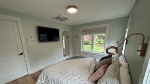 Una camera da letto con un letto, una TV a parete, una finestra con persiane e una luce a soffitto.