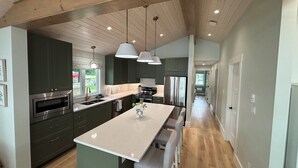 Una cucina moderna con mobili verde scuro, elettrodomestici in acciaio inossidabile e un'isola centrale con sgabelli da bar.