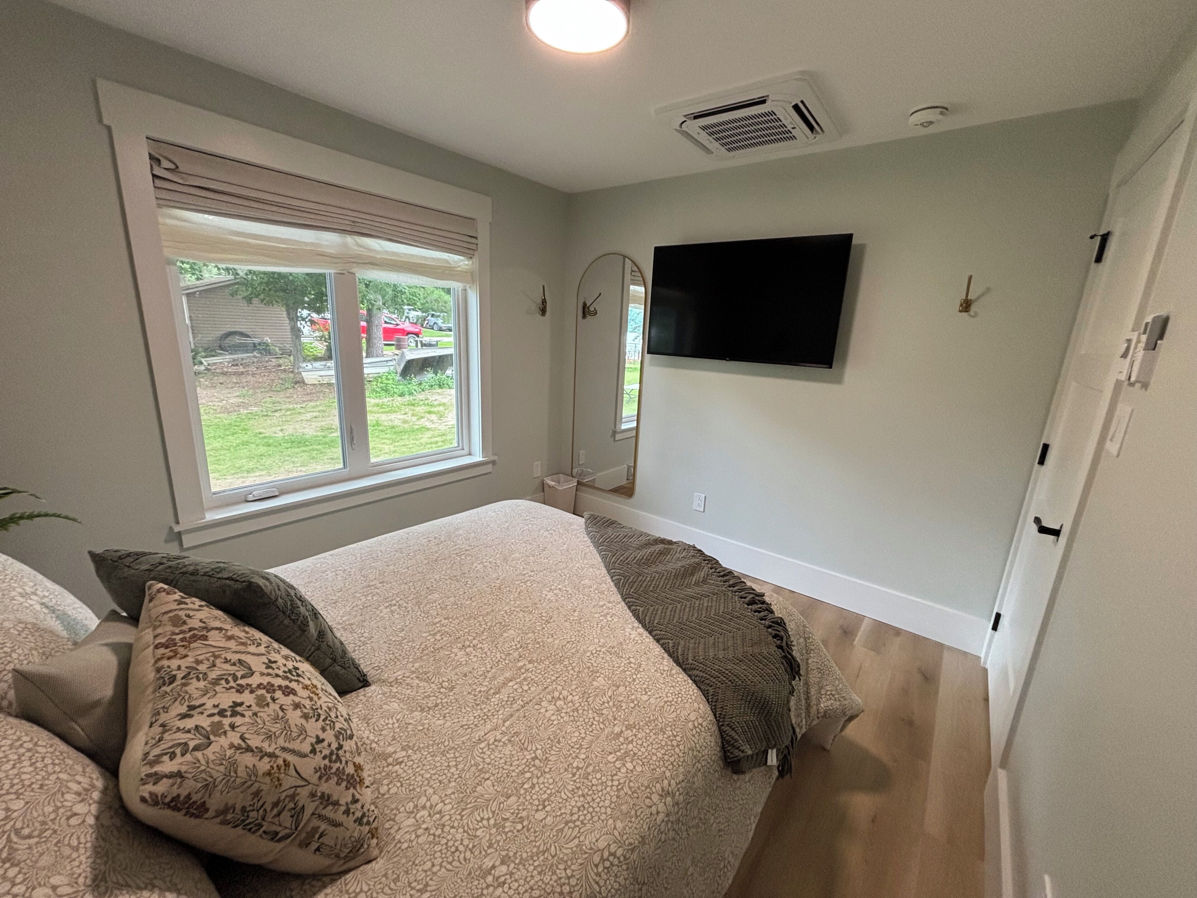 Ein Schlafzimmer mit Bett, Fenster, Flachbildfernseher und Spiegel.