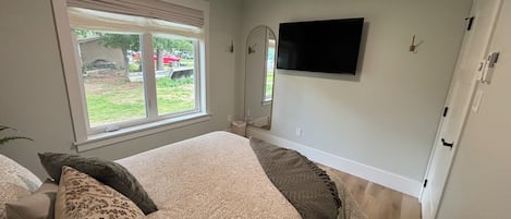 A bedroom with a bed, a window, a flat-screen TV, and a mirror.