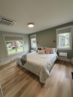 Une chambre avec un grand lit, deux fenêtres, une bouche d’aération au plafond et un radiateur.